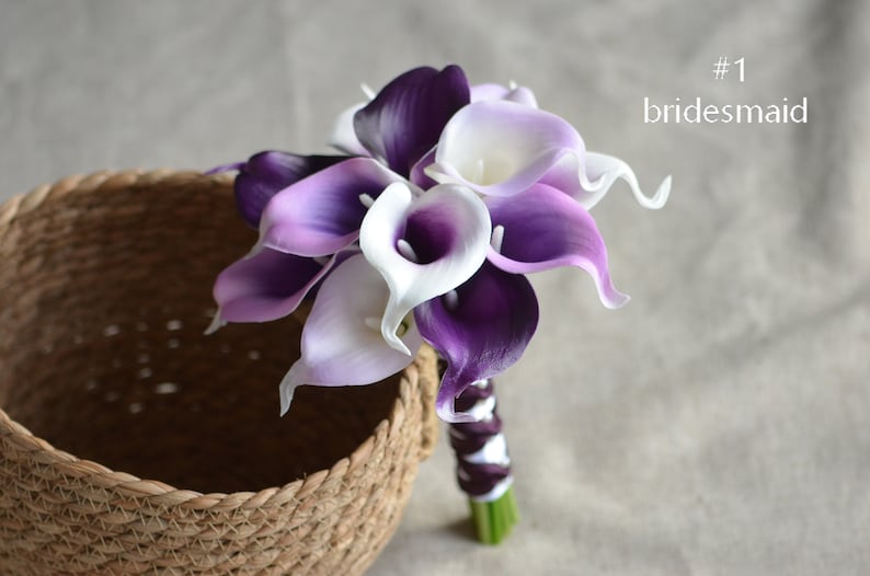 May include: A bouquet of purple and white calla lilies, tied with a purple ribbon. The bouquet is labeled "#1 bridesmaid".