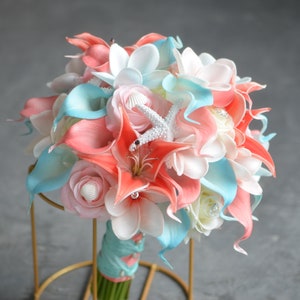 May include: A coral and blue bridal bouquet with white flowers and a starfish accent. The bouquet is arranged in a circular shape and is held together with a blue ribbon.