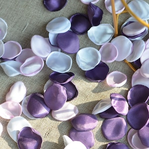 May include: Purple, white, and light pink silk flower petals scattered on a textured surface.