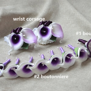May include: A set of purple and white calla lily boutonnieres and a wrist corsage. The boutonnieres have purple ribbon and the corsage has a white ribbon.