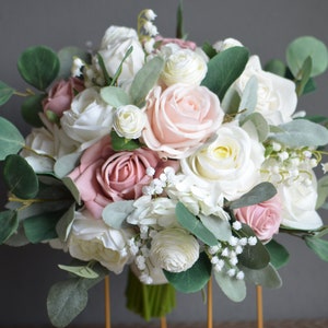 May include: A bridal bouquet featuring blush pink and white roses, eucalyptus, and baby's breath.