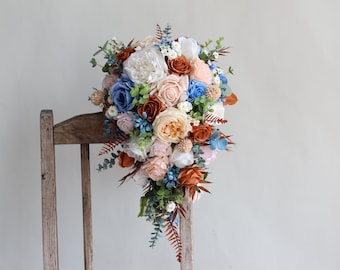 May include: A cascading bridal bouquet featuring a mix of peach, white, and blue flowers. The bouquet is crafted with silk flowers and has a rustic, vintage aesthetic.