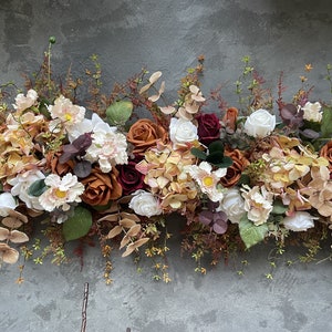 May include: A floral garland with a mix of white, burgundy, and orange roses, along with other flowers and greenery.