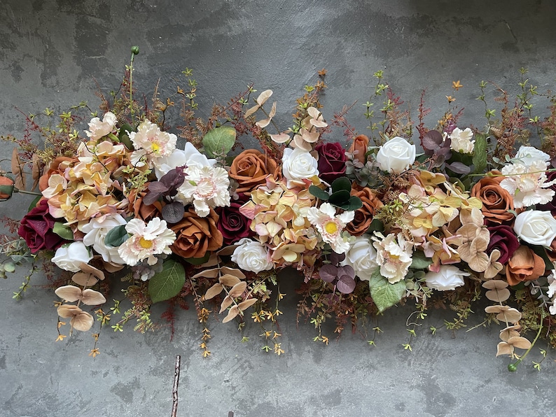 May include: A floral garland with a mix of white, burgundy, and orange roses, along with other flowers and greenery.