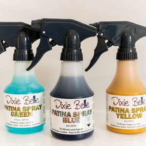 Może przedstawiać: Trzy butelki ze spryskiwaczem z etykietą Dixie Belle Patina Spray w kolorze zielonym, niebieskim i ż&oacute;łtym. Butelki mają pojemność 8 uncji (237 ml) i są przeznaczone do brązu i miedzi.