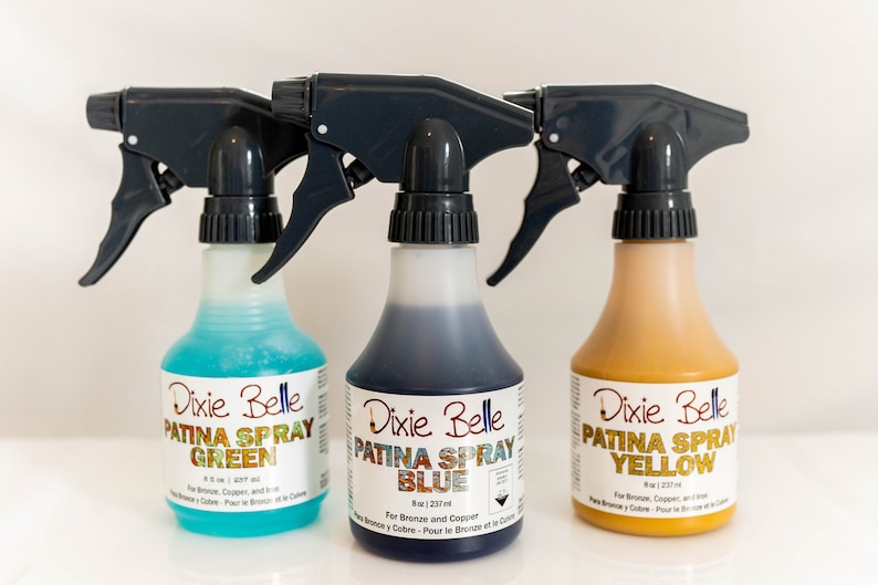 Może przedstawiać: Trzy butelki ze spryskiwaczem z etykietą Dixie Belle Patina Spray w kolorze zielonym, niebieskim i ż&oacute;łtym. Butelki mają pojemność 8 uncji (237 ml) i są przeznaczone do brązu i miedzi.
