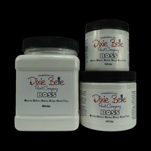 Op de afbeelding: Drie witte verfpotten met Dixie Belle Paint Company BOSS labels. De potten zijn gelabeld "Blocks Odors, Stains, Stops Bleed Thru White".