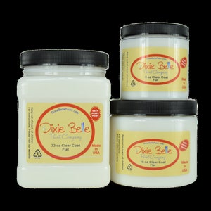 Puede incluir: Tres botes de pintura blanca con tapas negras. Los botes están etiquetados Dixie Belle Paint Company Clear Coat Flat. Los botes son de 8, 16 y 32 onzas.