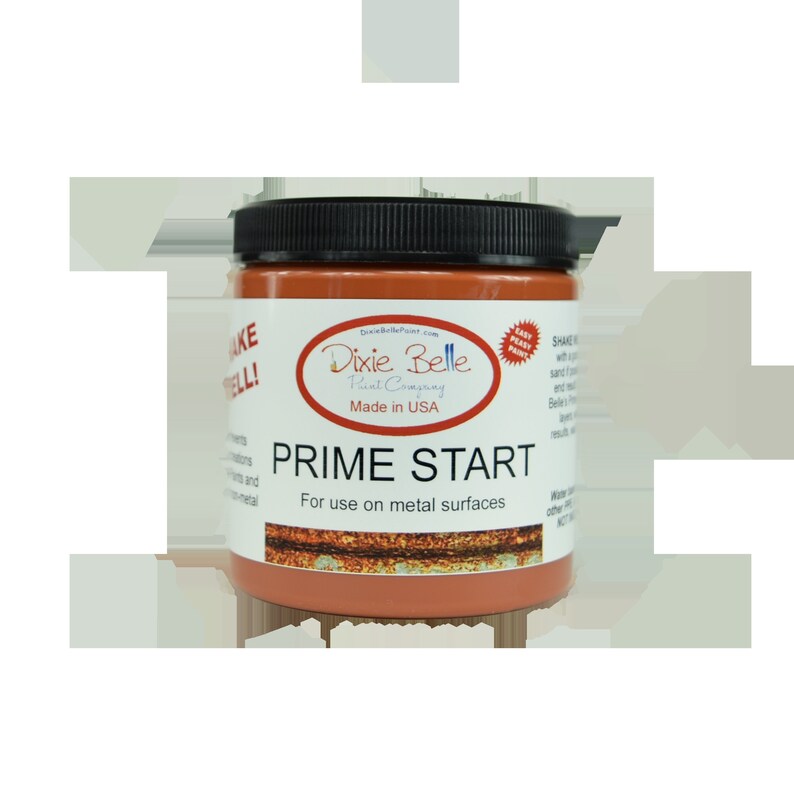 Może przedstawiać: Szklany słoik z podkładem Prime Start do powierzchni metalowych firmy Dixie Belle Paint Company. Słoik jest oznaczony logo firmy i nazwą produktu. Słoik ma rdzawo-pomarańczowy kolor.