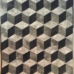 Op de afbeelding: Een zwart-wit geometrisch patroon quilt met een 3D kubusontwerp. De quilt is gemaakt van stof met een subtiel aquareleffect.