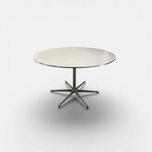 May include: A modern, round table with a white tabletop and a silver-colored, starburst-style base. The table is set against a plain white background, showcasing its minimalist design. The table's diameter is approximately 40 inches.