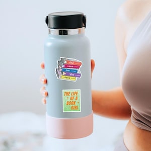 May include: A light blue water bottle with a black cap and a pink base. The bottle has two stickers: one with a stack of books labeled "Deal, Attitude, State, Goal, Legacy" and another with the text "The Life of a Book Girl".