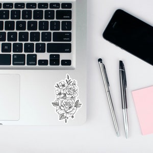 Peut inclure: Un autocollant blanc sur un ordinateur portable argent&eacute; avec un dessin au trait noir et blanc d'un bouquet de roses et d'autres fleurs.
