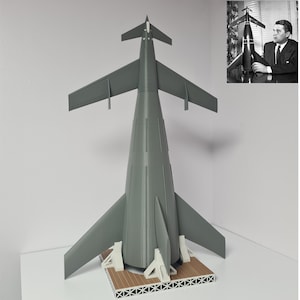 Op de afbeelding: Een grijs model van een raket met een puntige neuskegel en vleugels. De raket staat op een houten platform met een witte basis.