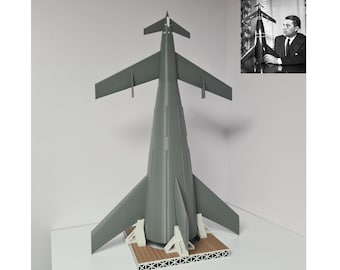 Könnte beinhalten: Ein graues Modell einer Rakete mit einer spitzen Nasenkappe und Flügeln. Die Rakete steht auf einer Holzplattform mit einem weißen Sockel.