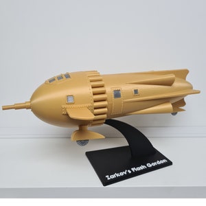 May include: A gold-colored model of a rocket ship, called "Zarkov's Flash Gordon", on a black stand.