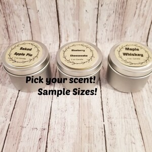 May include: Three small, silver sample-sized candles with labels reading "Baked Apple Pie", "Blueberry Cheesecake", and "Maple Whiskey". The text "Pick your scent! Sample Sizes!" is below the candles.