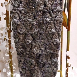 May include: A gray and blue crocheted leg warmer with a textured pattern. The leg warmer is displayed on a decorative metal stand with a distressed finish. The handmade item is likely for cold weather.