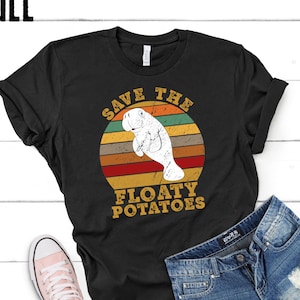 May include: Black t-shirt with a retro design featuring a manatee inside a circular graphic with horizontal stripes in shades of orange, brown, and red. The text reads "SAVE THE FLOATY POTATOES".