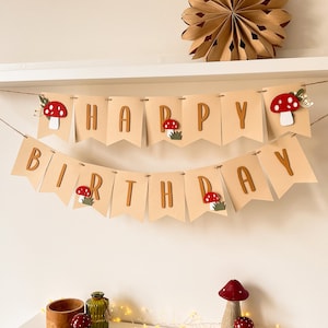 Puede incluir: Una pancarta de papel marrón con las palabras "Happy Birthday" en letras marrones. La pancarta está decorada con recortes de setas rojas y blancas.