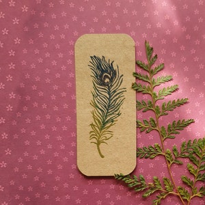 Peut inclure: Deux tampons en bois avec un motif de plume de paon. Un tampon est brun et l'autre est blanc avec de l'encre bleue et verte.