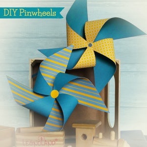 May include: Two DIY pinwheels, one with yellow and white checkered pattern and the other with yellow and blue stripes, both with teal blue blades. The pinwheels are on a wooden surface with the text "DIY Pinwheels" and "LEGOLAND" visible.