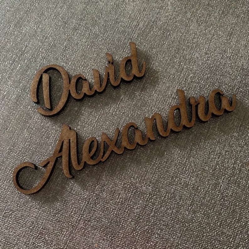 Op de afbeelding: Twee houten naamschildjes met de namen "David" en "Alexandra" in cursief.