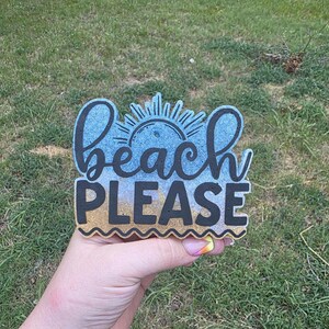 May include: A decorative sign featuring the text beach PLEASE in black lettering. The background has a gradient effect transitioning from a light blue sky color at the top to a sandy tan color at the bottom, with a sun graphic above the word beach.