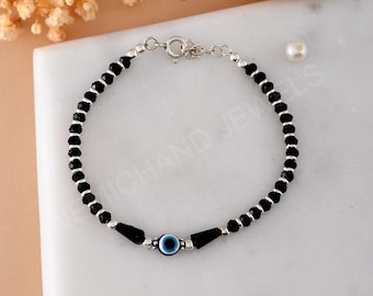 May include: A delicate bracelet featuring black beads and silver accents. The bracelet includes a central evil eye charm with blue and white details. The bracelet is approximately 7 inches in length and has a clasp closure.