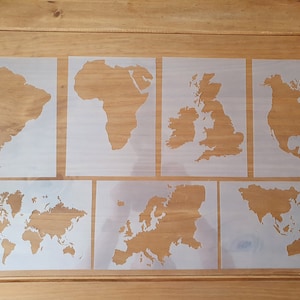 May include: A set of seven stencils depicting geographical outlines, including continents and a world map. The stencils are made from a translucent material and are laid out on a wooden surface. The continents include South America, Africa, the UK, North America, Europe, Asia, and the world.