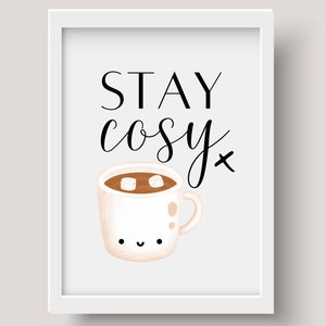 Puede incluir: Impresi&oacute;n enmarcada en blanco con texto negro que dice "STAY cosy" y una ilustraci&oacute;n de dibujos animados de una taza blanca con l&iacute;quido marr&oacute;n y dos malvaviscos blancos en su interior. La taza tiene una cara feliz.