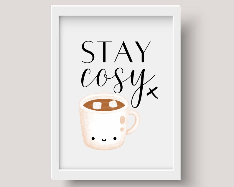 Puede incluir: Impresi&oacute;n enmarcada en blanco con texto negro que dice "STAY cosy" y una ilustraci&oacute;n de dibujos animados de una taza blanca con l&iacute;quido marr&oacute;n y dos malvaviscos blancos en su interior. La taza tiene una cara feliz.