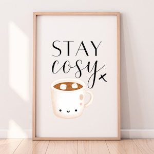 Puede incluir: Una impresi&oacute;n enmarcada en blanco con el texto "STAY cosy" en fuente cursiva negra. Debajo del texto hay una ilustraci&oacute;n de dibujos animados de una taza blanca con un l&iacute;quido marr&oacute;n y malvaviscos blancos en su interior.