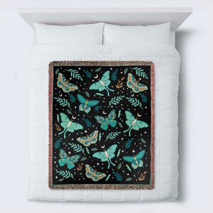 May include: A woven throw blanket with a black background and a repeating pattern of green and blue moths, leaves, and stars.