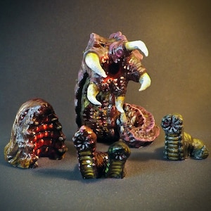 May include: A set of five miniature, hand-painted, fantasy creature figurines. The main figure is a purple and brown worm-like creature with a large mouth and sharp teeth. The other four figures are smaller, brown and green worm-like creatures.