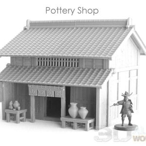 Puede incluir: Un modelo impreso en 3D gris de una tienda de cerámica japonesa con un techo de tejas, paredes de madera y un letrero que dice "Pottery Shop". La tienda tiene un pequeño porche con una mesa y sillas, y hay varias macetas en exhibición.