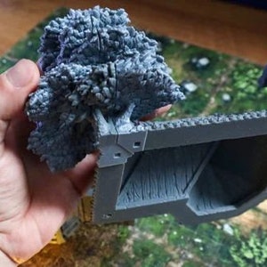 Puede incluir: Una miniatura de un edificio de piedra impreso en 3D de color gris con un techo texturizado y un peque&ntilde;o &aacute;rbol en frente.