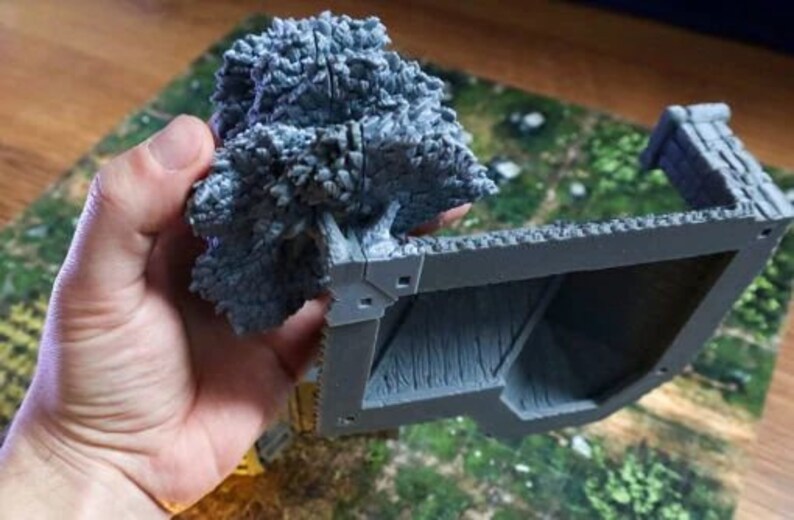 Puede incluir: Una miniatura de un edificio de piedra impreso en 3D de color gris con un techo texturizado y un peque&ntilde;o &aacute;rbol en frente.