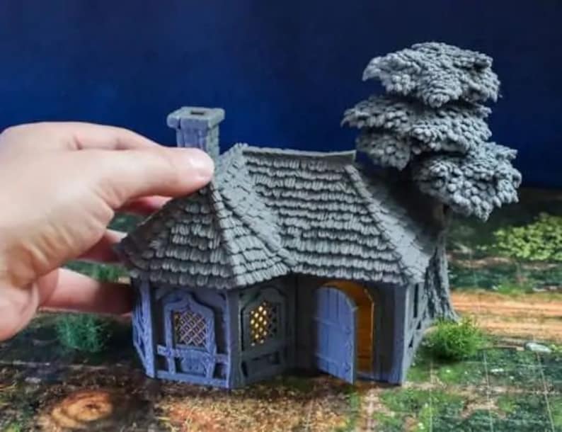 Puede incluir: Una caba&ntilde;a en miniatura gris con techo de paja, una peque&ntilde;a puerta y ventanas. Un &aacute;rbol en miniatura gris est&aacute; al lado de la caba&ntilde;a.