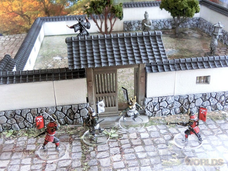 May include: A miniature Japanese garden scene with a white wall, a gate, and several figures. The figures are painted in black, red, and gold. The scene is set on a gray stone path.