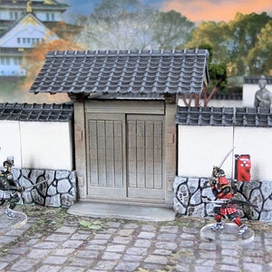 May include: A miniature Japanese castle gate with two wooden doors, a gray tiled roof, and white walls. Two miniature figures of samurai warriors stand in front of the gate.