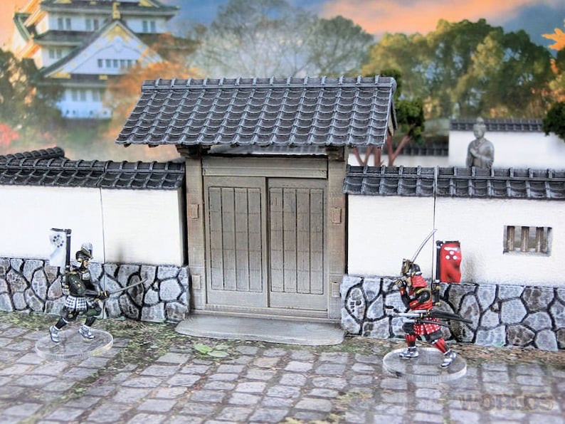 May include: A miniature Japanese castle gate with two wooden doors, a gray tiled roof, and white walls. Two miniature figures of samurai warriors stand in front of the gate.