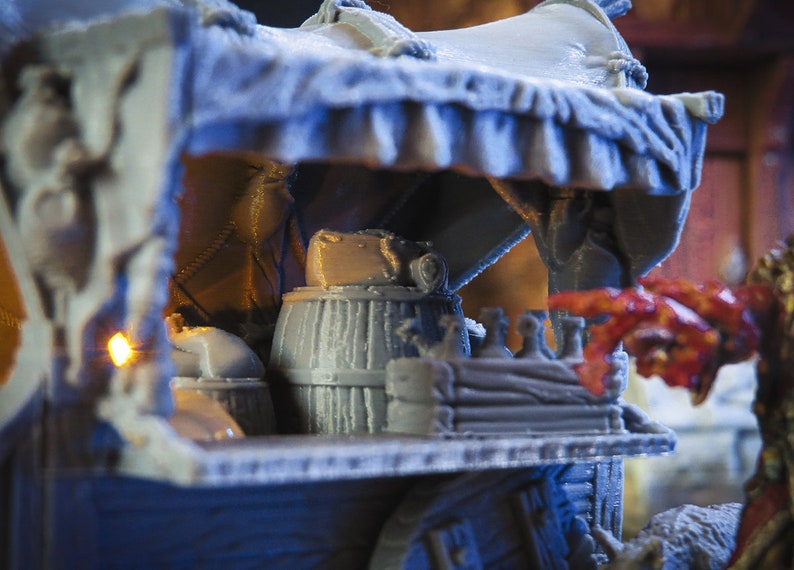 May include: A miniature wooden wagon with a canvas awning, a barrel, and other supplies. The wagon is painted in a light grey colour and has a wooden wheel.