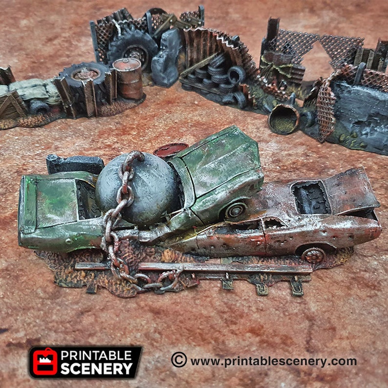 May include: A green and rusty car is crushed by a large metal ball and chain. The car is sitting on a dirt surface with a metal fence in the background.  www.printablescenery.com