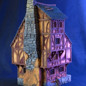 Puede incluir: Un modelo en miniatura de un edificio de tres pisos con una chimenea de piedra, un marco de madera y un techo de color p&uacute;rpura. El edificio tiene varias ventanas y una peque&ntilde;a puerta. Una figura en miniatura se encuentra frente al edificio.