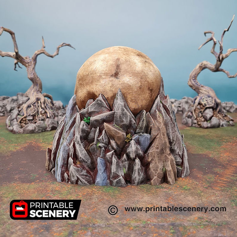 May include: A 3D printed miniature mountain with a golden orb on top. The mountain is made of textured gray and brown rock with green foliage. The orb is smooth and shiny.