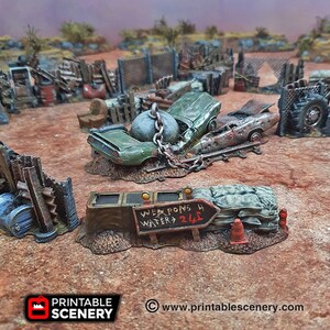 May include: A miniature model of a post-apocalyptic wasteland scene with a wrecked car, a chain-link fence, and a sign that reads "Weapons 4 Water 24/7".