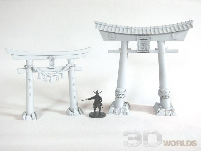 May include: Two white painted miniature Japanese Torii gates. The larger gate is taller and wider than the smaller gate. Both gates have a traditional design with a curved top and two vertical pillars.