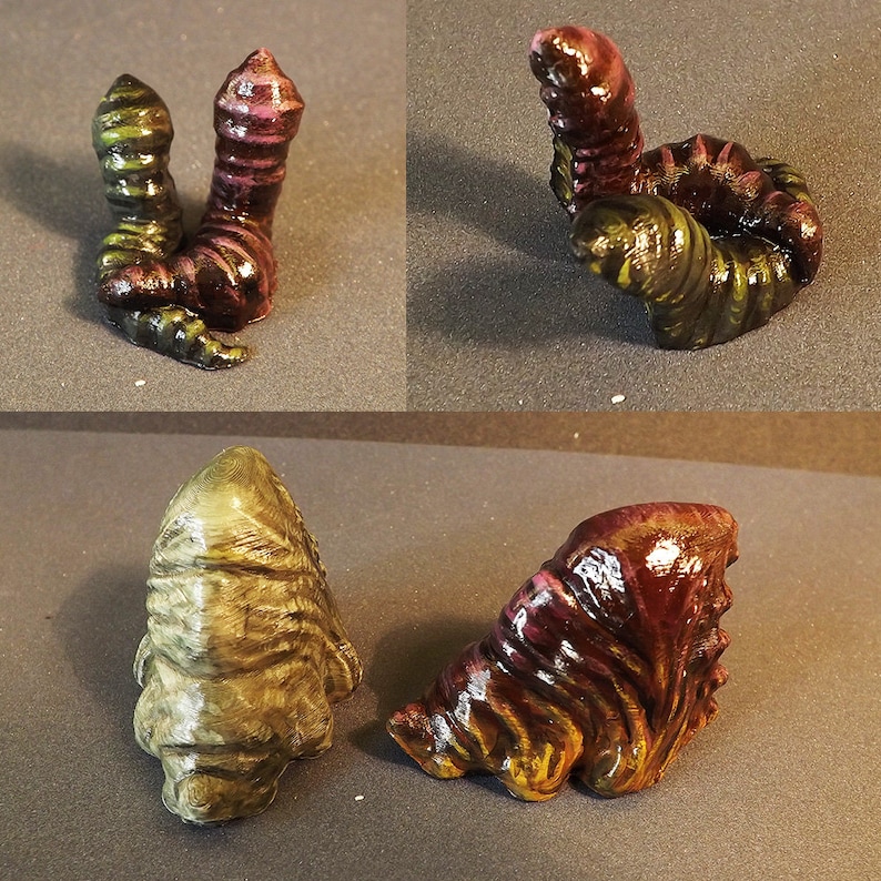 May include: Four 3D printed alien creature figurines. Two are green and brown with a striped pattern. One is a dark brown and purple with a striped pattern. The last one is a dark brown and purple with a striped pattern and is curled up.