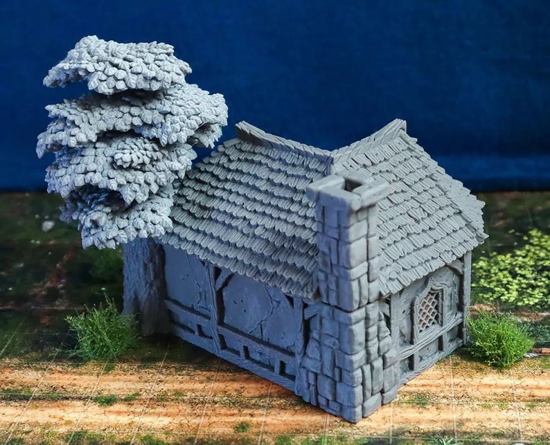 Puede incluir: Una caba&ntilde;a de piedra gris en miniatura con un techo de paja y un peque&ntilde;o &aacute;rbol a su lado. La caba&ntilde;a tiene una ventana con un dise&ntilde;o de celos&iacute;a y una chimenea. El modelo est&aacute; hecho de un material texturizado y est&aacute; dise&ntilde;ado para juegos de mesa o exhibici&oacute;n en miniatura.